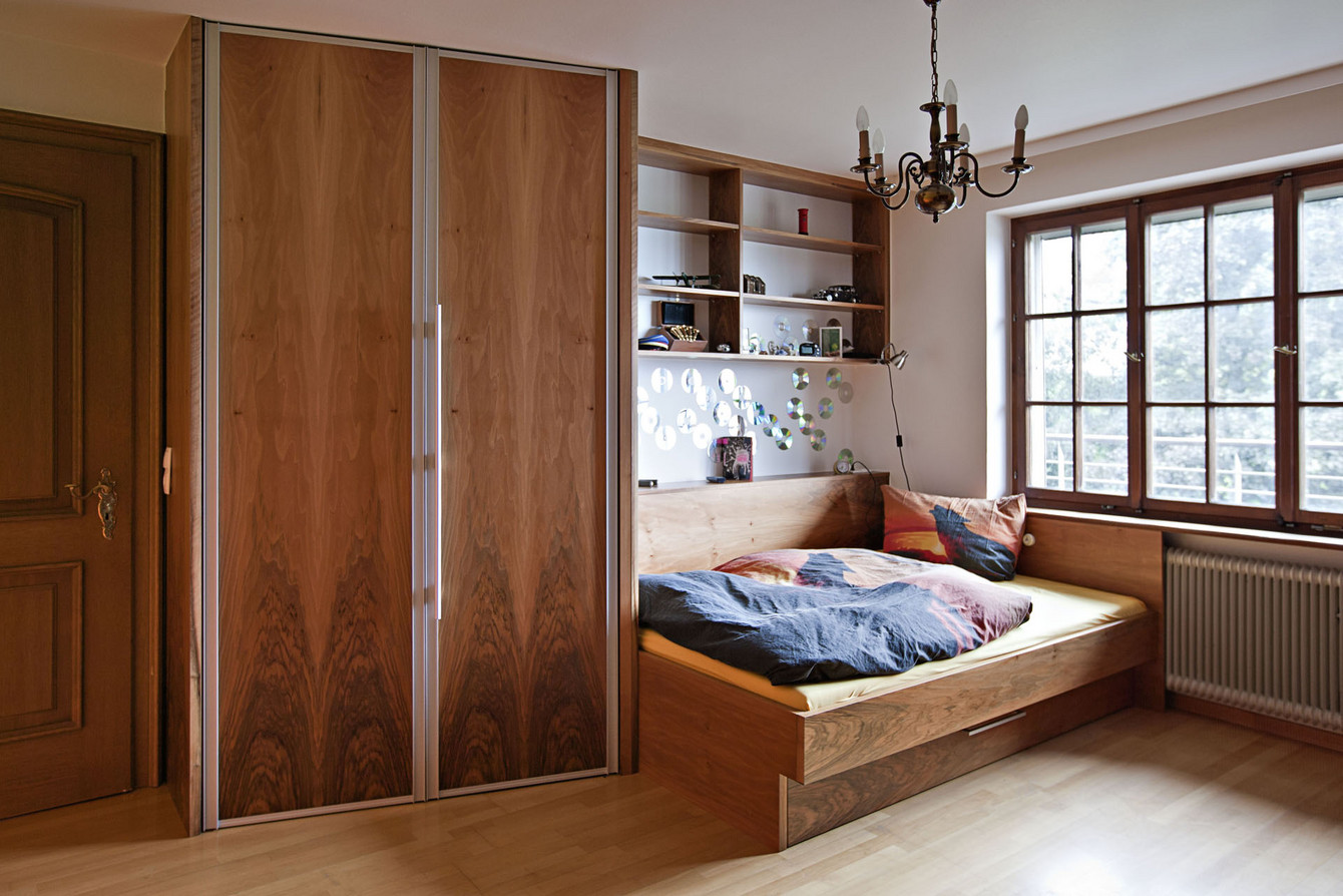 Jugendzimmer mit Falttürenschrank, Bett mit Unterschublade und Wandregal in Nussholz furniert