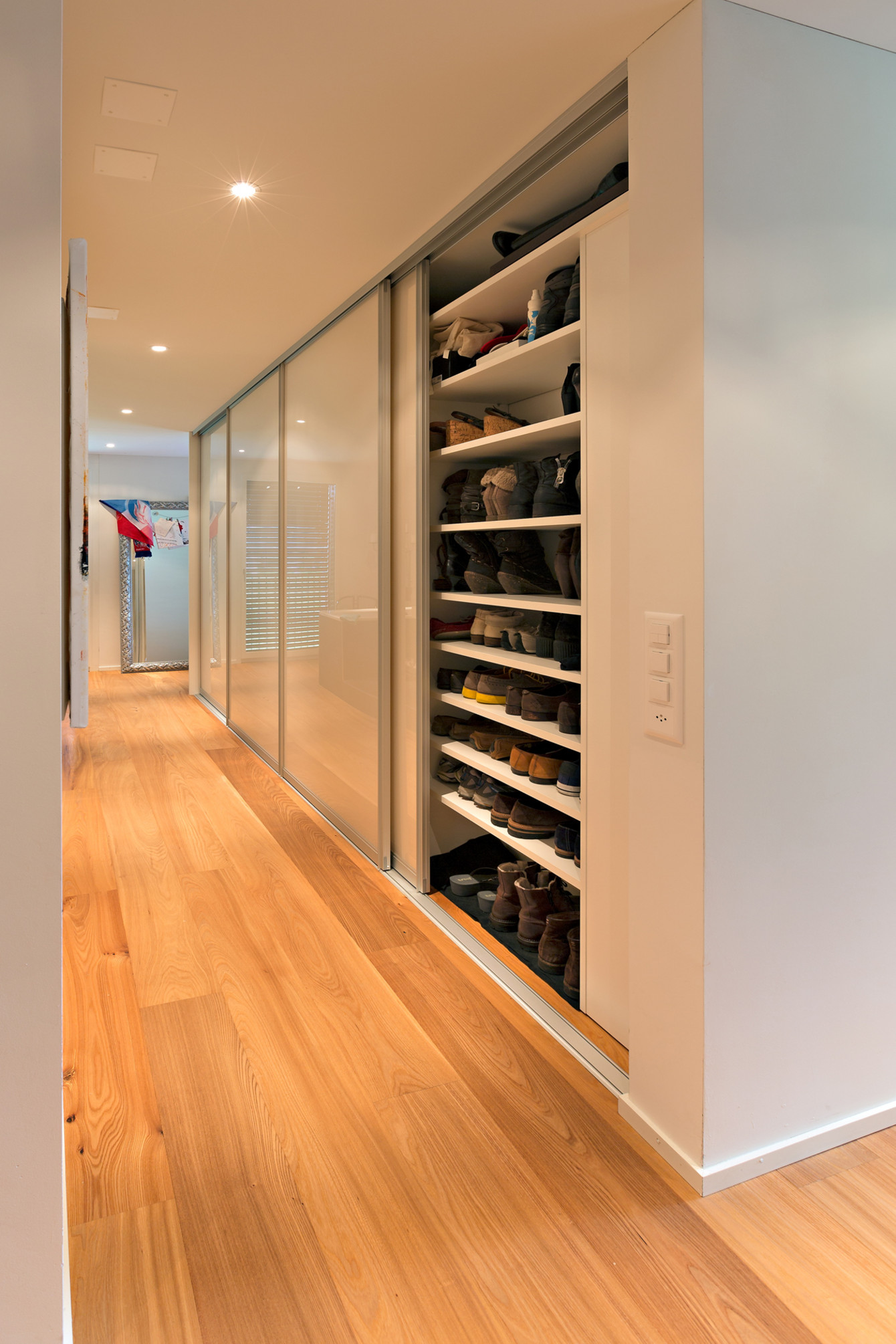 Schuhschrank über die ganze Raumhöhe hinter Schiebetüren in Acrylglas weiss mit Aluprofilen 