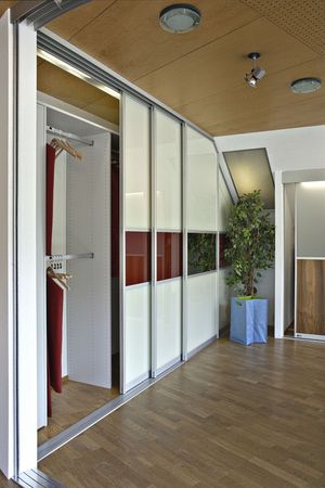 Mehrtüriger Schiebetürenschrank mit Türfüllung in extraweissem Glas mit rotem Qurstreifen und seitlich abfallender Schiebetüre an die Dachneigung des Raumes