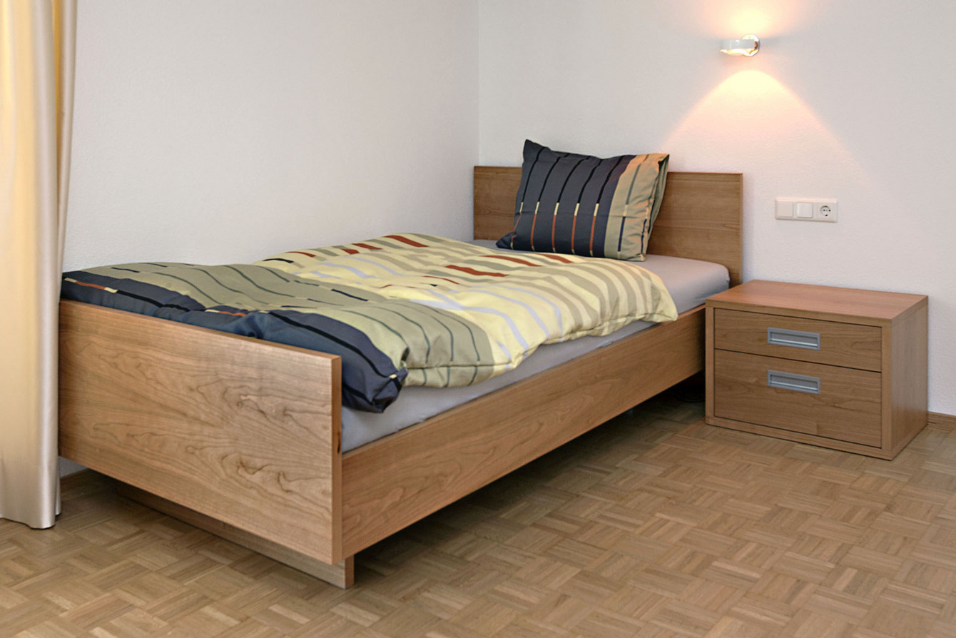 Jugendbett in Holz für die Matratzengbreite von 1.40 m mit freistehendem passendem Nachtkasten mit Schubladen im gleichen Holz 